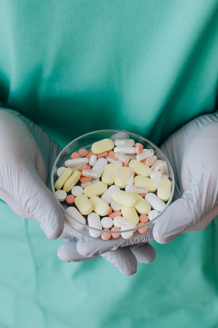 Crop anonymous medical worker in rubber disposable gloves with bowl of assorted pills in hands